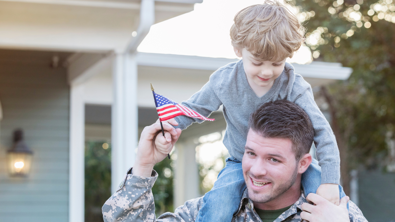 Military service member with child on shoulders holding American flag